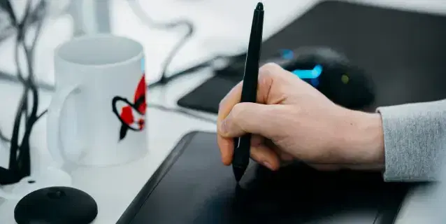 Zbliżenie na dłoń podczas pracy na tablecie graficznym i kubek z logiem Mighty Koi